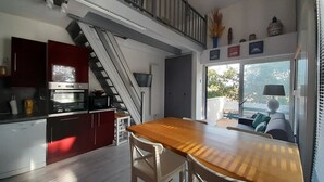 A modern kitchen with a wooden table and chairs, a staircase, and a view of the outdoors. - Spacious T2 duplex in a wooded residence 5 minutes from the beach and the center (Andernos-les-Bains)