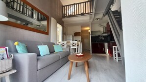 A living room with a grey sofa, wooden coffee table, and a staircase leading to an upper level. - Spacious T2 duplex in a wooded residence 5 minutes from the beach and the center (Andernos-les-Bains)