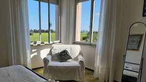 Una stanza con un letto, una sedia e una finestra vista su un campo verde.