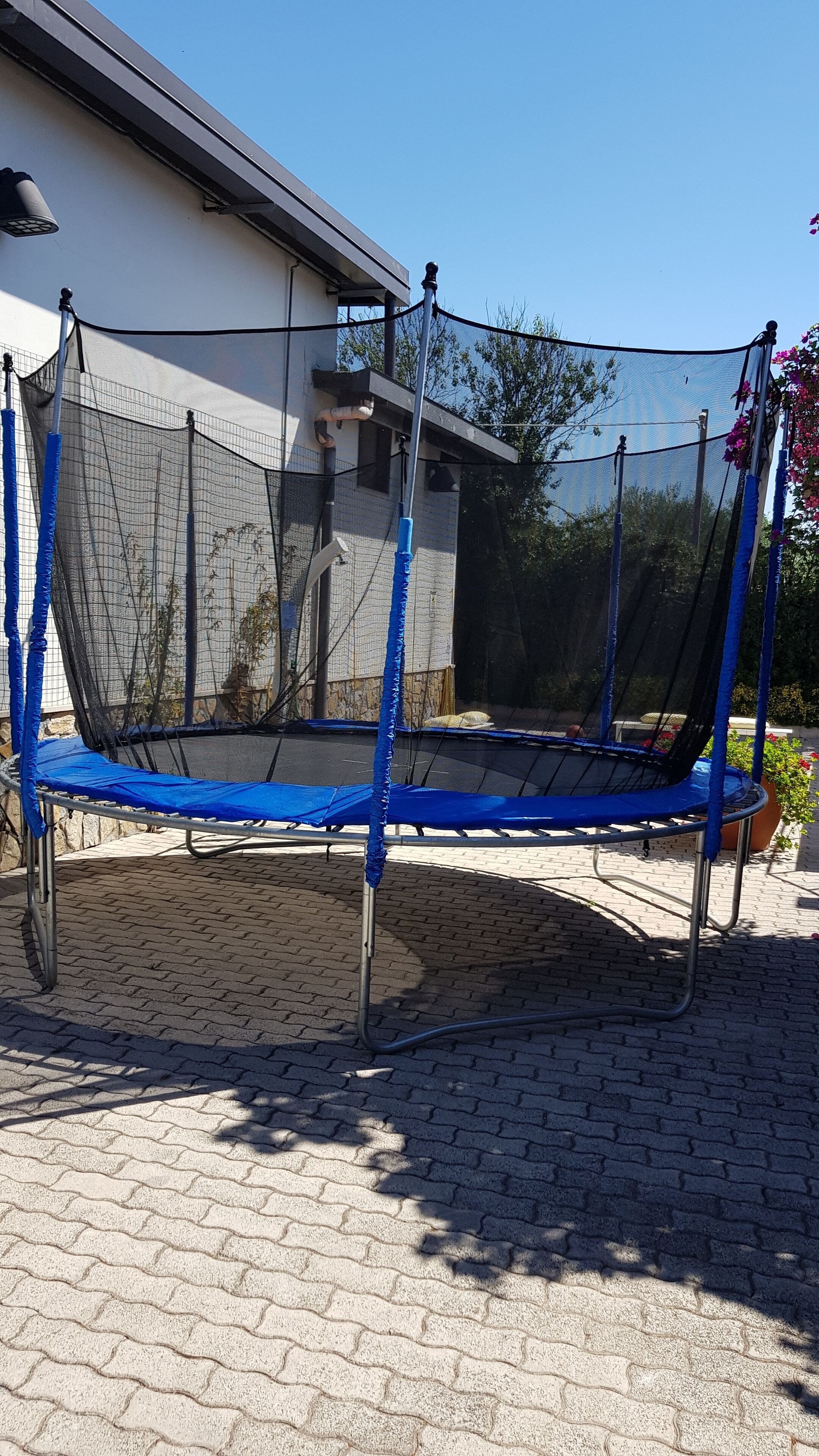 A trampoline with a safety net, set on a paved patio with a house in the background.