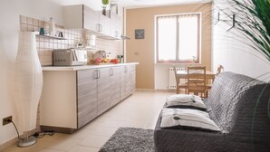 Une cuisine moderne avec des meubles blancs, un coin repas comprenant une table et des chaises, et un canapé gris dans un espace de vie lumineux.