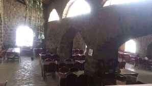 A stone-walled room with arched ceilings and tables and chairs arranged for dining.