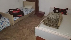 A room with two single beds, one with a polka dot bedspread and the other with a leopard print bedspread. There is a small wooden nightstand with a lamp between the beds.