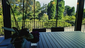 Ein Balkon mit Tisch und Stühlen, einer Blumenvase und Blick auf ein bewaldetes Gebiet.