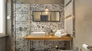 A bathroom with a patterned tile wall, a wooden vanity, a mirror, a shower, and a sink. - Mediceo 42 - Comfort Double Room with Balcony (Pisa)