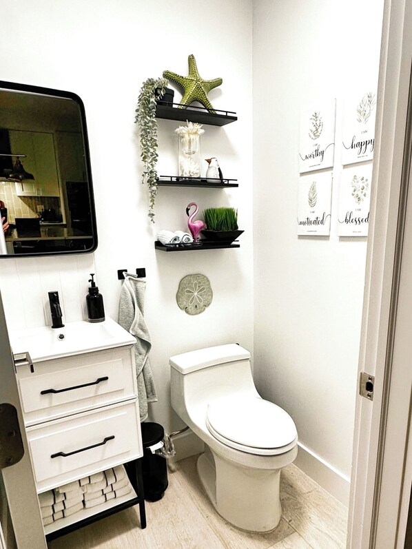 A bathroom with a white sink, a mirror, a toilet, and shelves with decorative items.