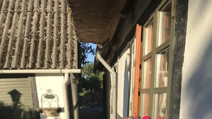 A narrow brick pathway leading to a building with a tiled roof and a window with a flower box.