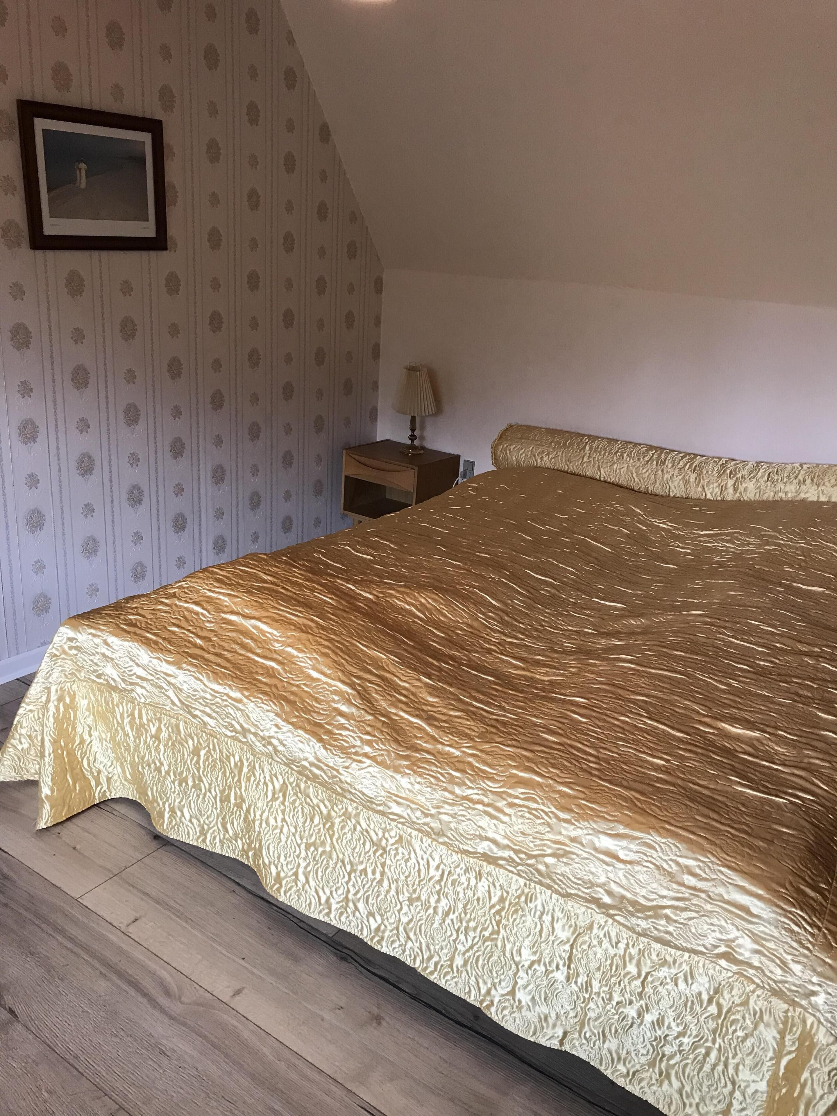 A bedroom with a large bed, a nightstand, a lamp, and a framed picture on the wall.
