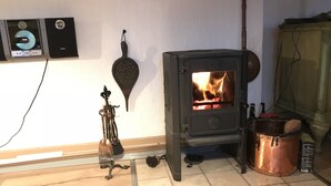 A room with a wood-burning stove, a wall-mounted heater, a broom, and a copper pot.