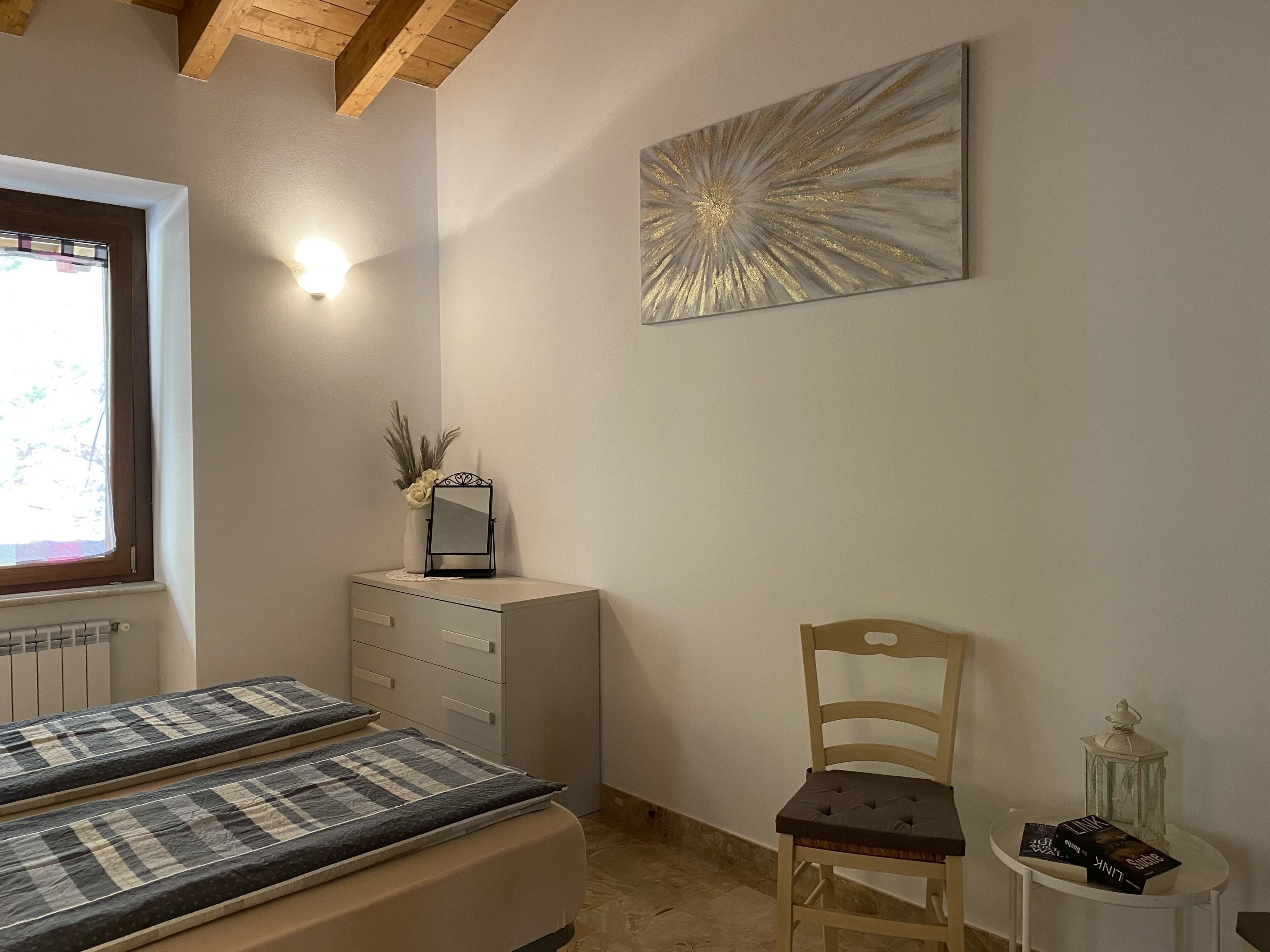 A bedroom with a bed, a chair, a dresser, a mirror, a wall art piece, and a window.
