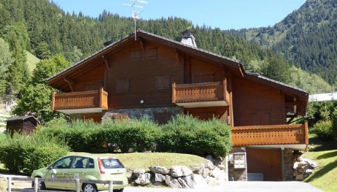 Una cabaña de madera con balcón, con montañas al fondo.