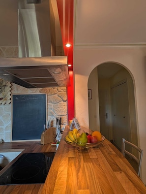 Une cuisine avec un plan de travail en bois, un panier de fruits, un tableau noir sur lequel est écrit « Bienvenue ! », et une bande lumineuse rouge.