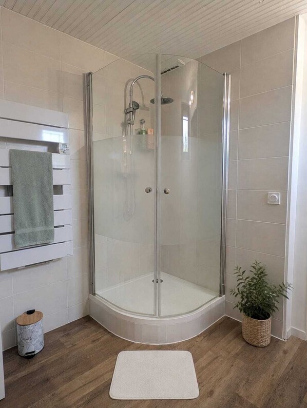 A glass-enclosed shower with a white tiled wall and a wooden floor.