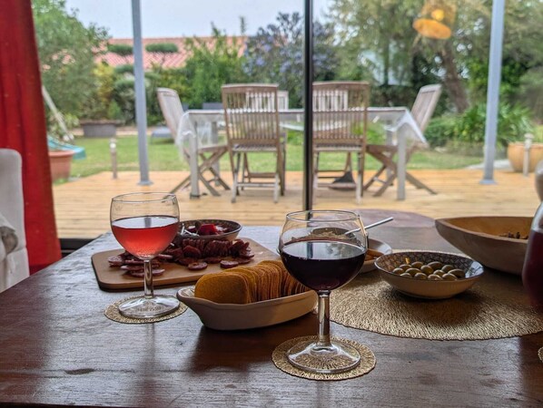 An outdoor dining area with a table set for two, featuring a glass of red wine, a bowl of olives, and a plate of cured meats.