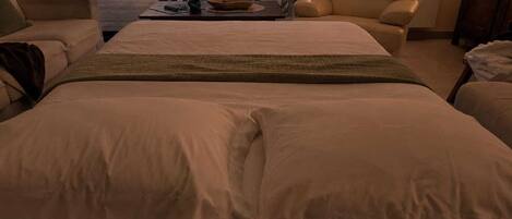 A bedroom with a large bed, two chairs, a small table, and a view of the outdoors.