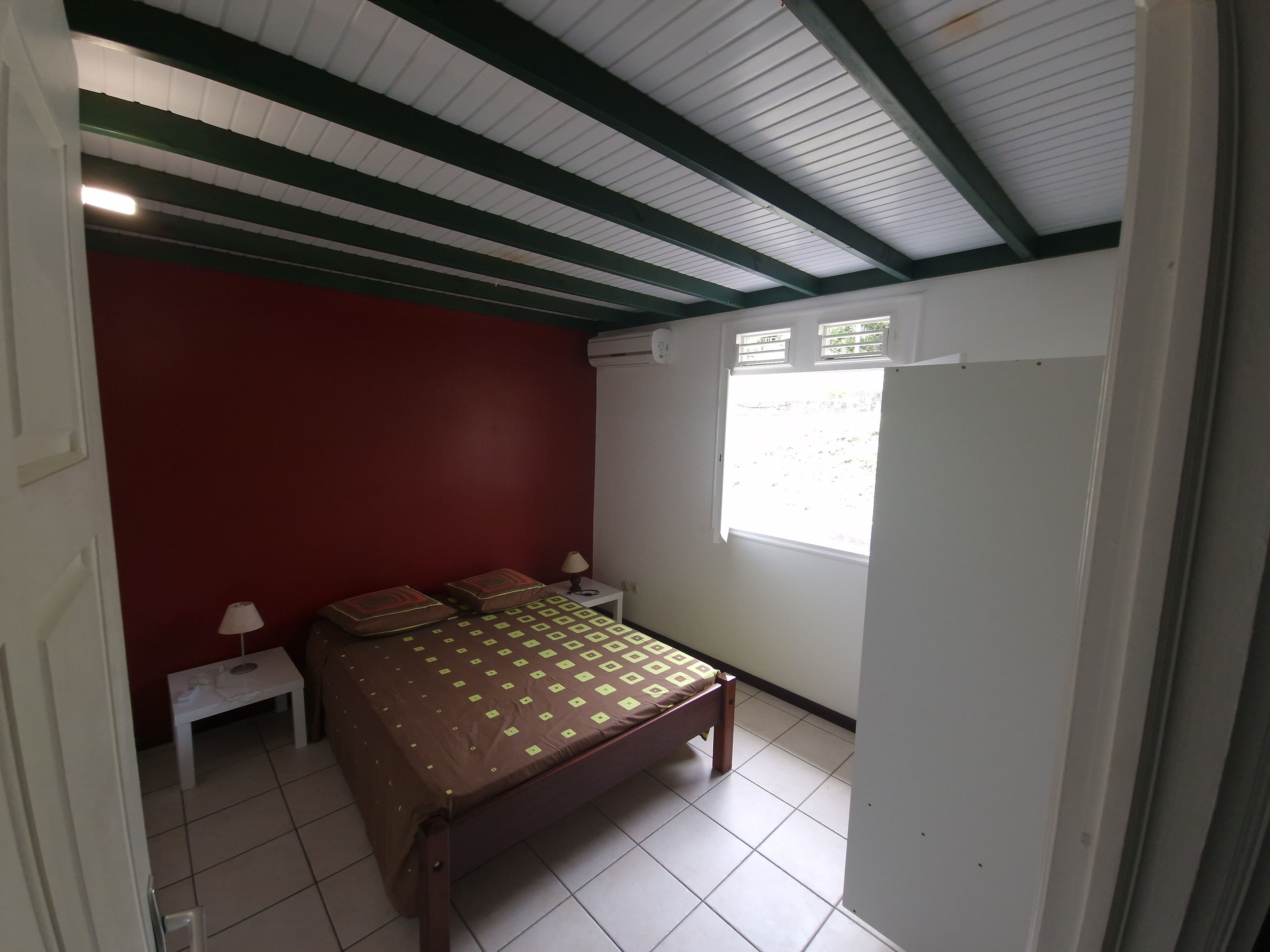 A bedroom with a bed, a nightstand, a window, and a red wall.