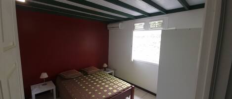 A bedroom with a bed, a nightstand, a window, and a red wall.