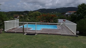 Piscina rectangular con valla blanca, rodeada de césped y árboles.