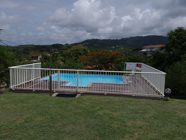 A rectangular swimming pool with a white fence, surrounded by a grassy area and trees. - Villa with Pool F3 south Martinique between mountain and sea (Le Vauclin)