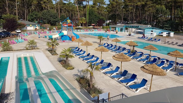 A resort with multiple swimming pools, a water slide, lounge chairs, and a tropical setting. - Mobile home in the Landes, view of the forest (Saint-Julien-en-Born)