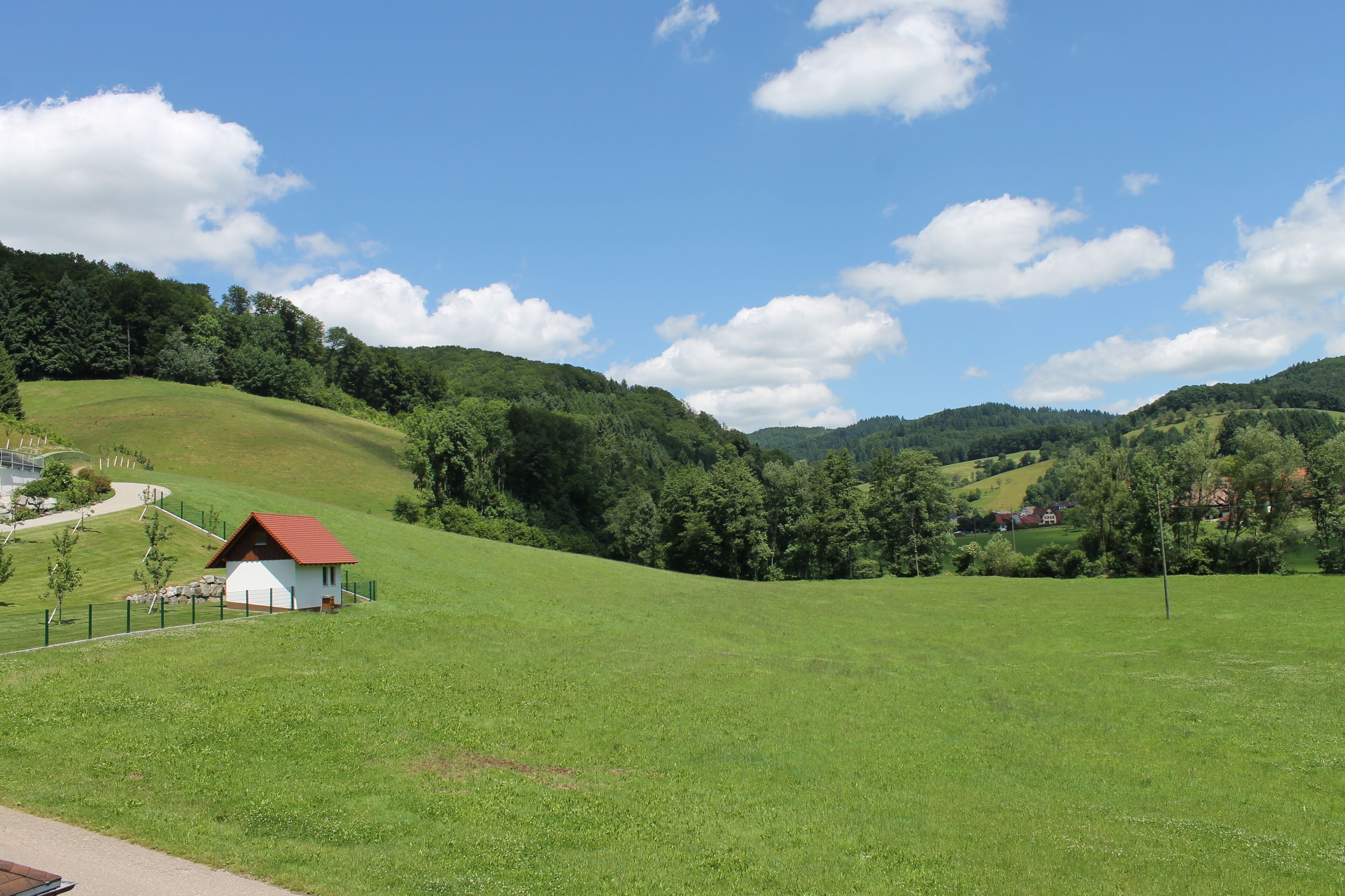 Eine ländliche Landschaft mit einem kleinen weißen Gebäude mit rotem Dach, umgeben von grünen Feldern und Hügeln.