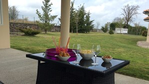 Un patio esterno con un tavolo in vetro, ciotole piene di snack e bicchieri da vino.