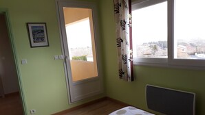 Una stanza con un letto, una finestra con tende, un termosifone e una porta che dà su un'altra stanza.