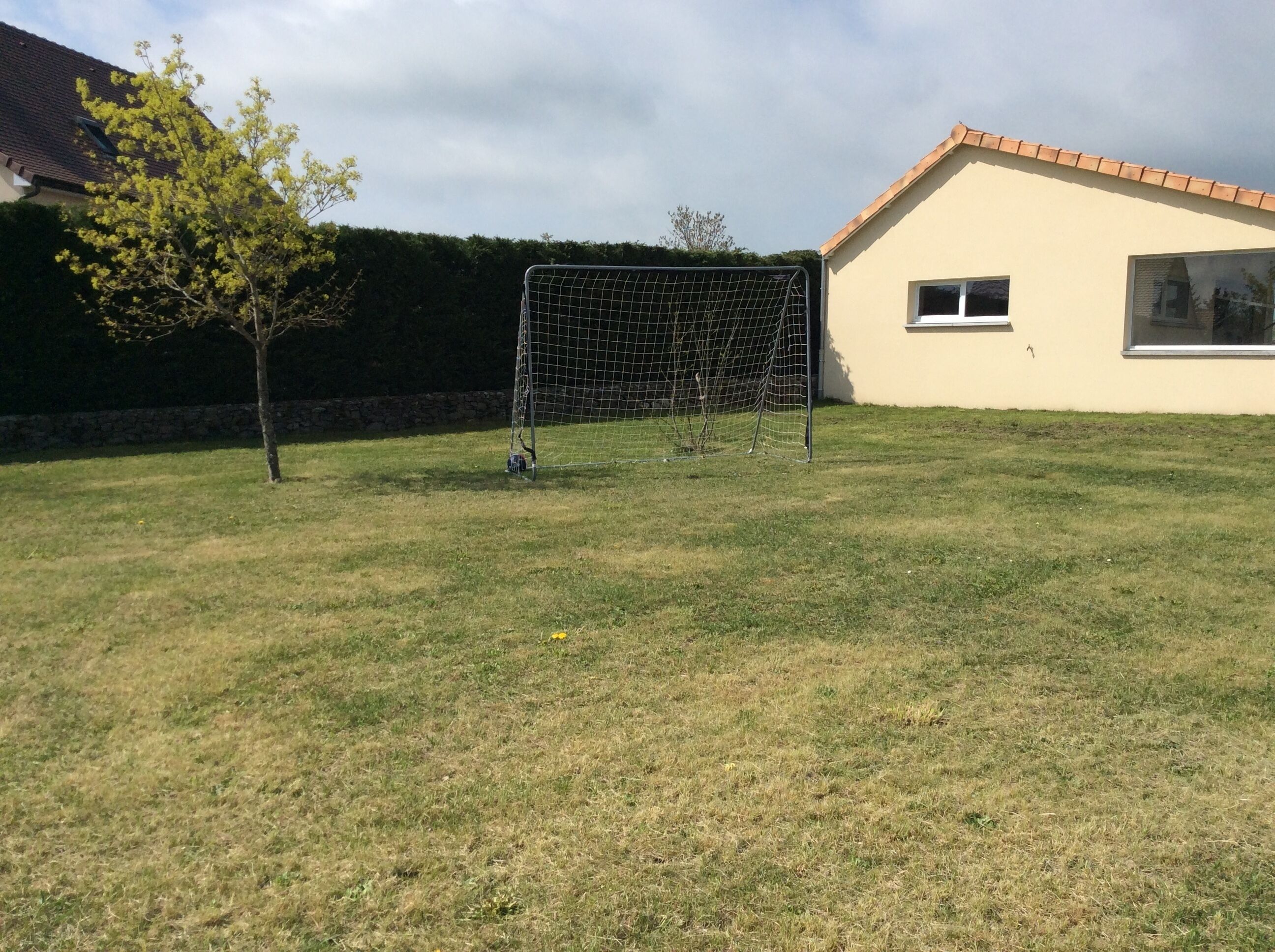 A grassy area with a soccer goal, a tree, and a building with a tiled roof.