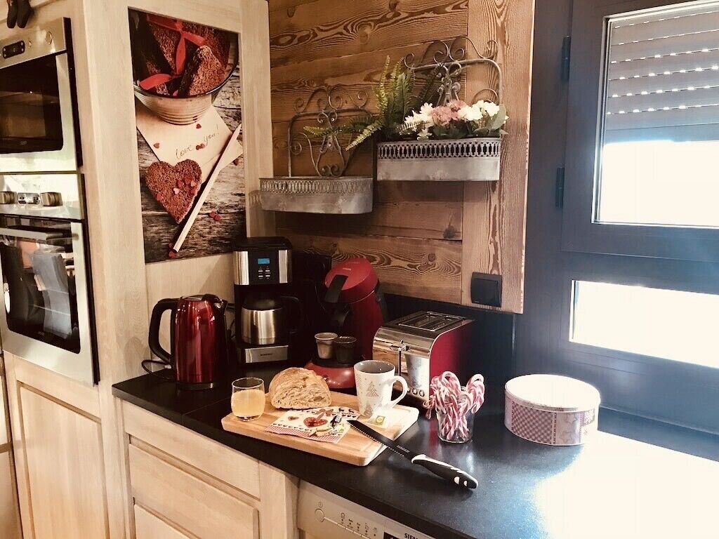Una cuina amb un rebedor de fusta, una cafetera, un torrador de pa i una taula de tall amb aliments.