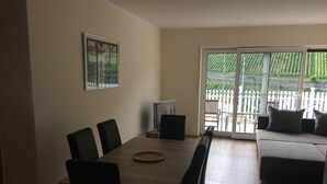 Un comedor con mesa y sillas, un sofá y un ventanal corredera que da a un jardín.