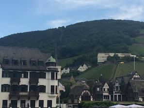 Un pueblo europeo tradicional con edificios históricos, incluyendo un edificio blanco destacado con techo verde y un balcón, y casas con entramado de madera y techos pronunciados.