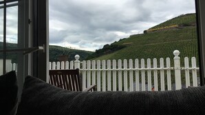 Vista desde una ventana con cerca blanca de piquetes, una silla y un letrero que dice "ASSMANNSHAUS HÖLLENBERG" en una ladera.