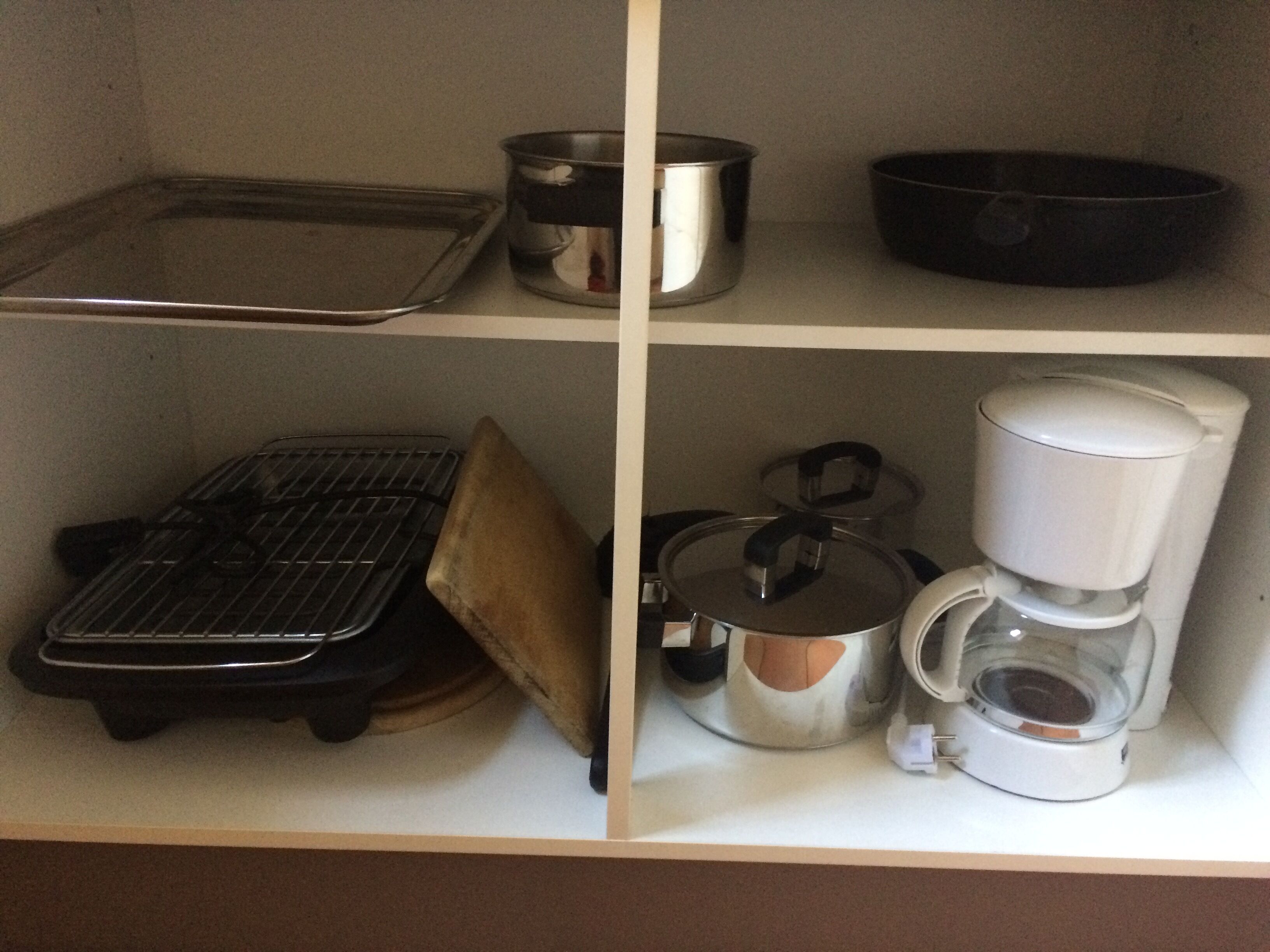 A kitchen shelf with various cookware including a baking tray, pots, a pan, and a coffee maker.