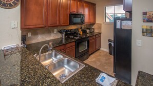A kitchen with granite countertops, stainless steel sinks, wooden cabinets, a black refrigerator, and a microwave. - Bella Piazza 912 - 234 (Davenport)