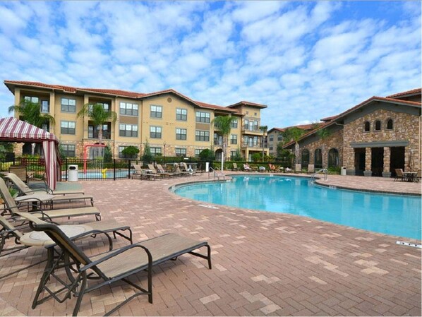 A hotel with a swimming pool, lounge chairs, and a brick patio.