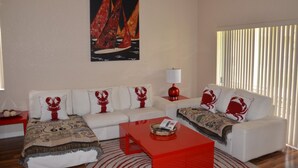 A living room with a white sofa set, a red coffee table, and a painting of sailboats on the wall. - Regal Palms Resort & Spa 1307 (Davenport)