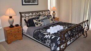A neatly made bed with a floral bedspread, two bedside tables with lamps, a framed cityscape picture on the wall, and a window with blinds. - Regal Palms Resort & Spa 1307 (Davenport)