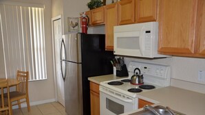A kitchen with wooden cabinets, a stainless steel refrigerator, a black freezer, a white microwave, a stove, and a sink. - Regal Palms Resort & Spa 1307 (Davenport)