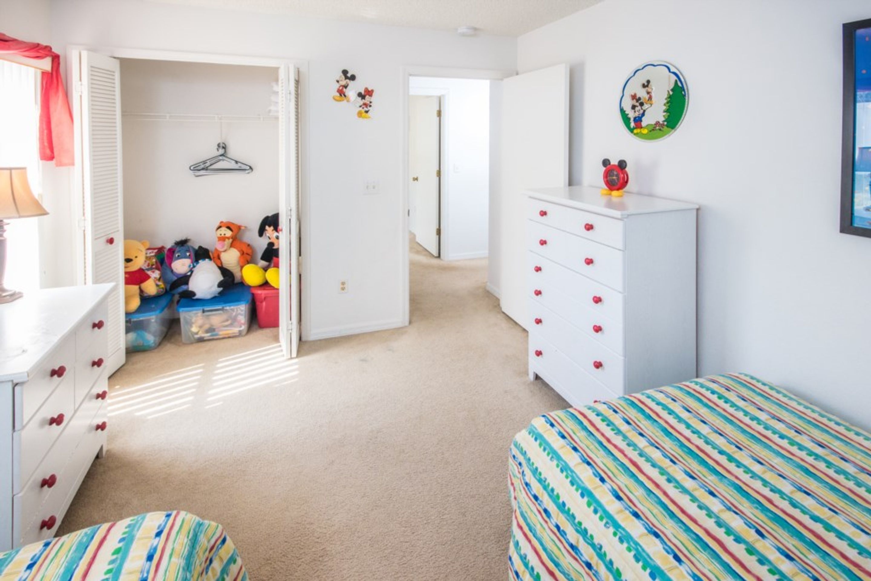 A child's bedroom with bunk beds, a dresser, a closet with stuffed toys, and wall decorations.
