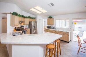 A modern kitchen with wooden cabinets, a large island with stools, and a view to the outside. - Lindfields 2930 (Kissimmee)