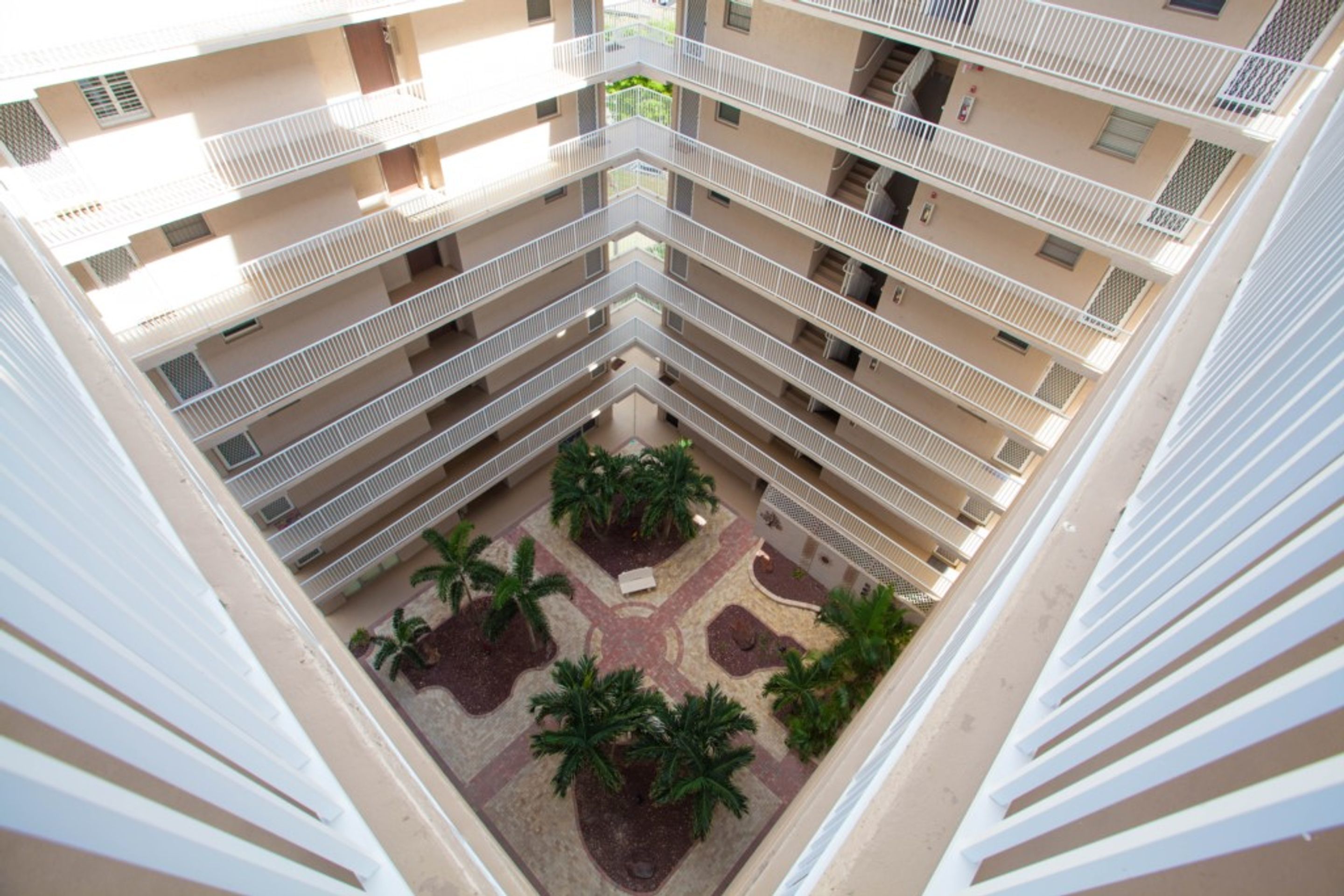 A multi-level atrium with balconies, a central courtyard with palm trees, and a beige building facade.