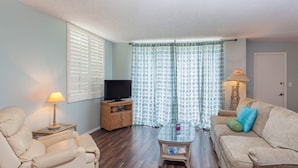 Una sala de estar con sofá, sillón, televisor y una mesa con lámpara.