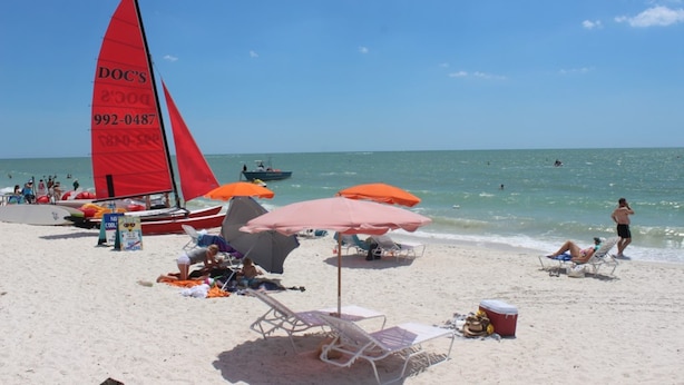 Una playa con un velero, sombrillas y sillas de descanso.