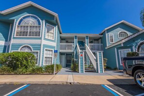 A two-story building with a blue exterior, a front entrance with a staircase, and a parking area with blue lines.
