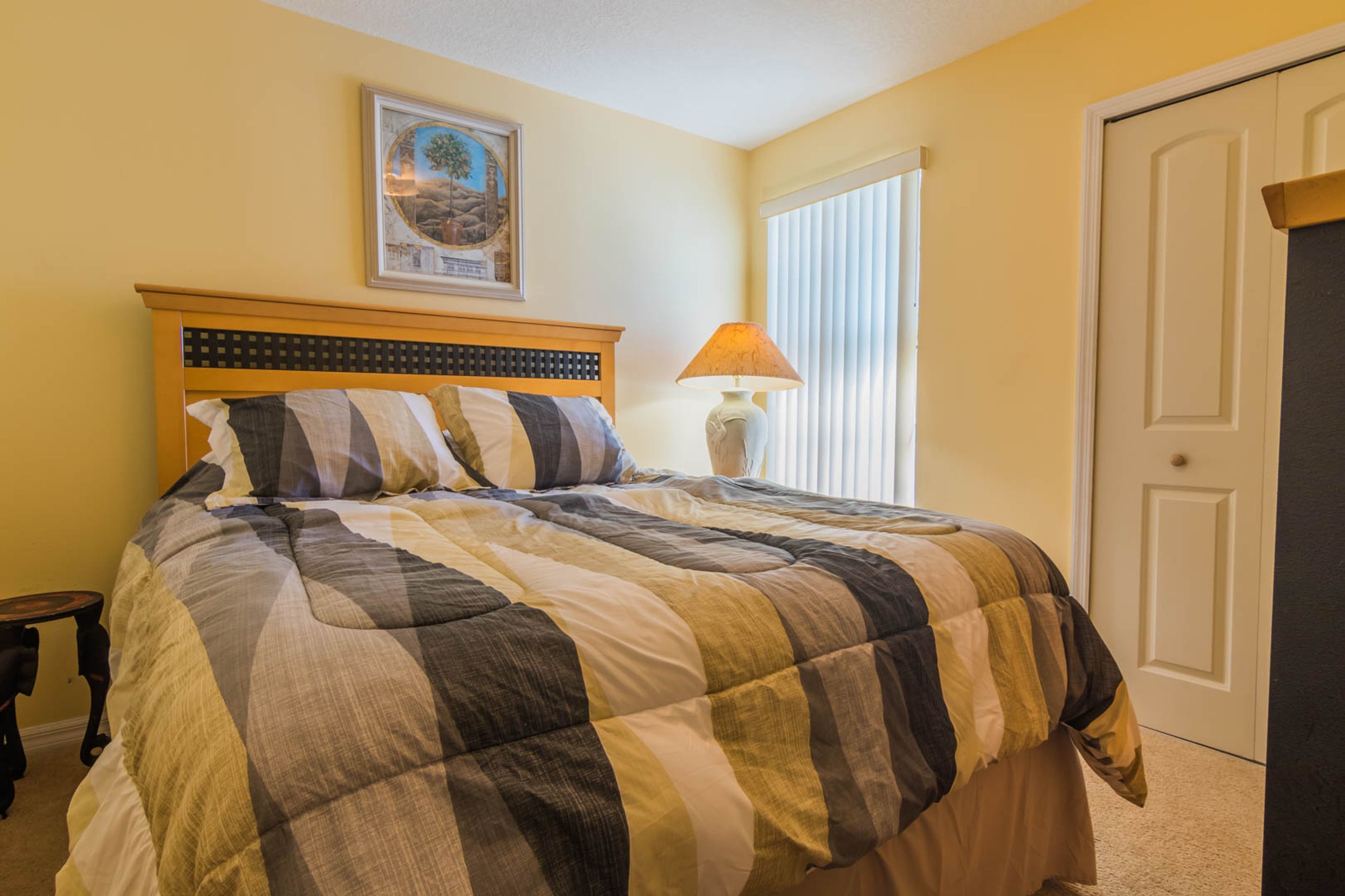 A bedroom with a bed, a nightstand, a lamp, a door, and a framed picture on the wall.