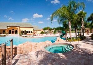 A swimming pool area with a building in the background, palm trees, and a water slide.