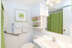 A bathroom with a white sink, a toilet, a green shower curtain, and a framed picture on the wall.