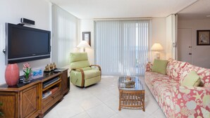 A living room with a flat-screen TV, a green armchair, a glass coffee table, and a floral sofa. - Bonita Beach 5500 - 1906 (Bonita Springs)