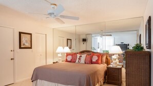 A bedroom with a bed, bedside tables, a nightstand, a mirror, a ceiling fan, and a door. - Bonita Beach 5500 - 1906 (Bonita Springs)