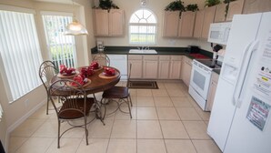 A kitchen with a dining table set for four, a white refrigerator, and wooden cabinets. - Indian Creek 2612 (Kissimmee)
